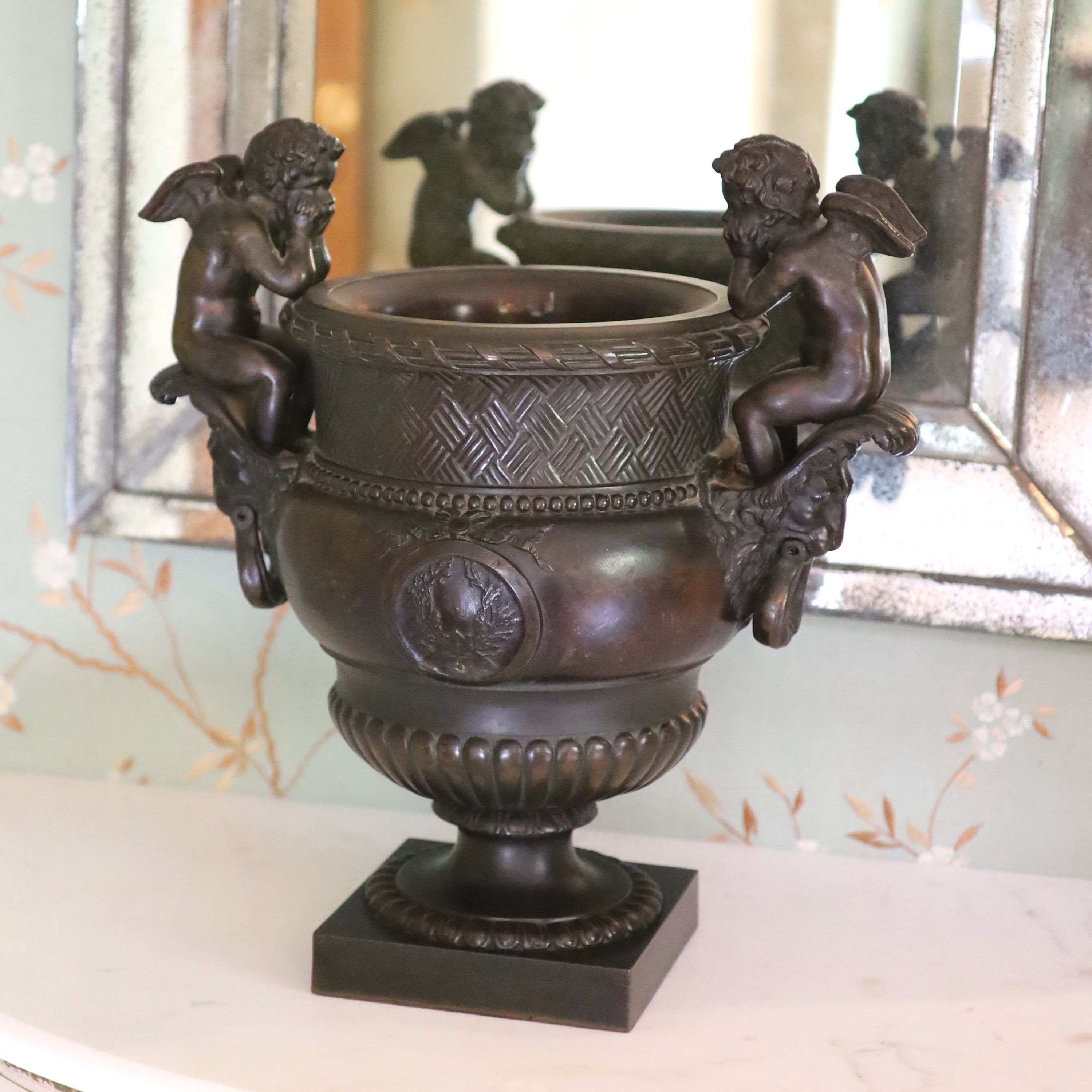 A classical style bronze urn modelled with disconsulate cherubs, height 44cm width 40cm